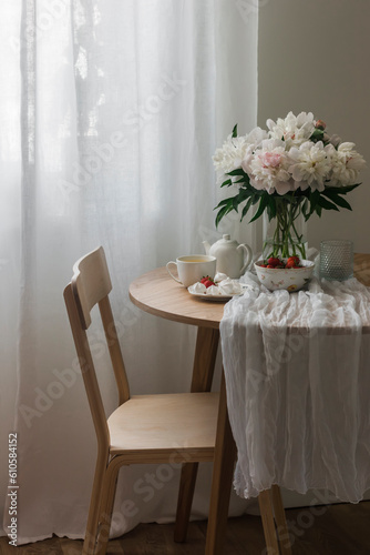 Tea party table - green tea, strawberries, meringue on a round wooden table, wooden chair, bouquet of peonies © okkijan2010