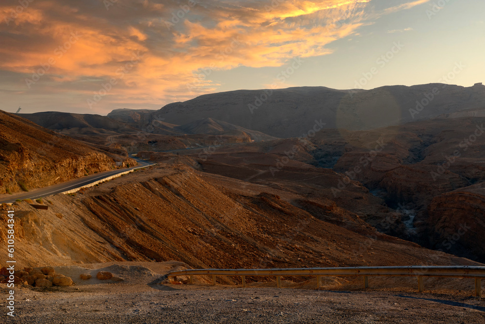 Mountains at sunset. Mountain road. Landscape with rocks, sky with clouds and beautiful asphalt road in the evening in summer. Travel background. Highway in mountains. Landscape in the evening