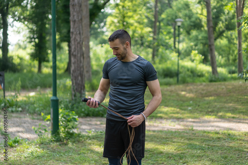 Close up photo of a young man holding a jump rope and training outside 