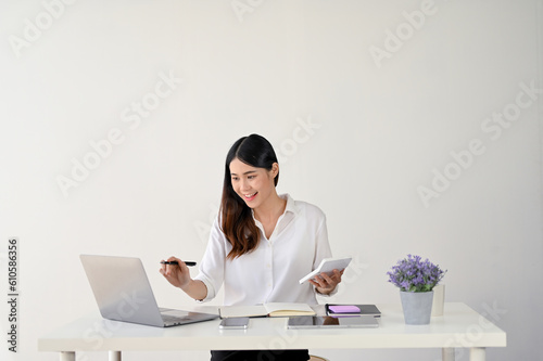 A businesswoman pointing her pen at her laptop screen while sitting at her desk.