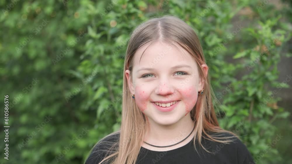 Cheerful girl with a dirty face after she ate strawberries in the garden. She is looking at the camera and smiling.