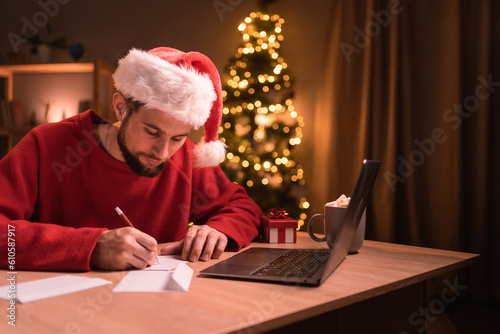 Men wearing Santa hat writing greeting cards at home office during christmas