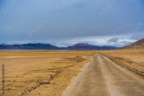 withered grass field, snow covered mountains, cloudy sky at the way from Moriri lake to Leh city, Ladakh, India