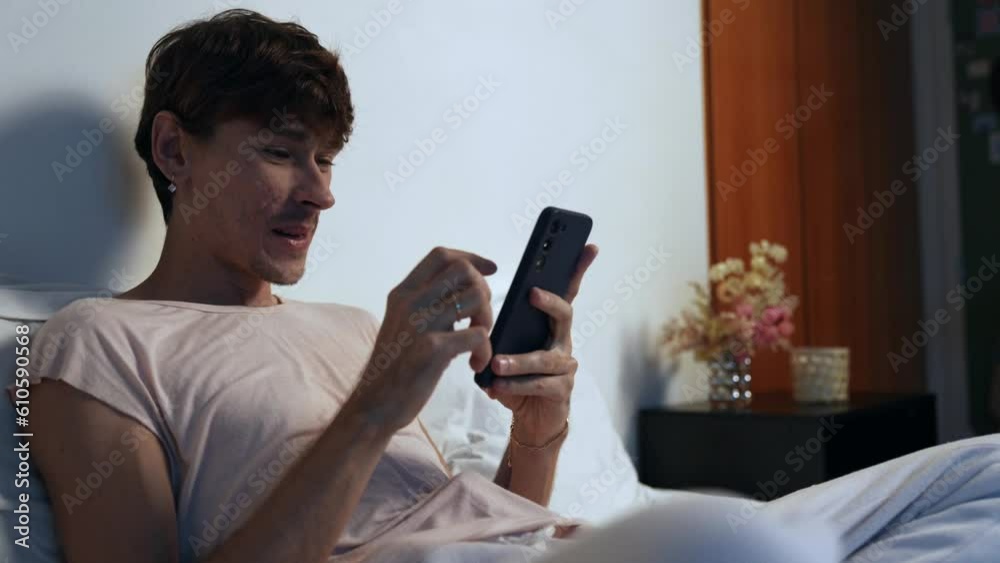 homem branco jovem brasileiro sentado na cama usando o celular no dia dos namorados