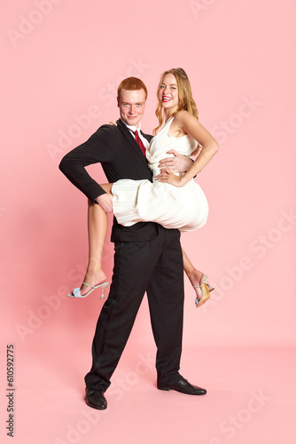 Young beautiful woman and handsome man got married, posing together against pink studio background. Happiness. Delightful. Concept of family, relationship, youth, emotions, fun. Ad