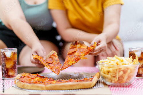 Happy oversize fat Asian women enjoy eating a pizza, hamburger, and French fry with drinking cola soda together. Unhealthy eating and unhealthy lifestyles concept.