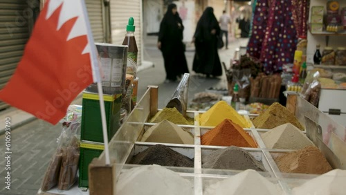 On a market stall in Manama in Bahrain, spices are sculpted into pyramid shapes. Two women wearing burkas walk towards the stall. 