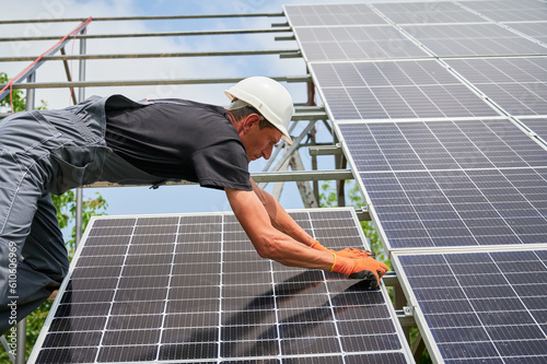 Cropped view of man engineer solar installer placing solar module on metal rails. Male worker installing photovoltaic solar panel system. Concept of alternative energy and power sustainable resources.