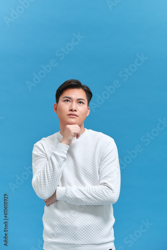 man thinking with hand touching chin in isolated studio blue background