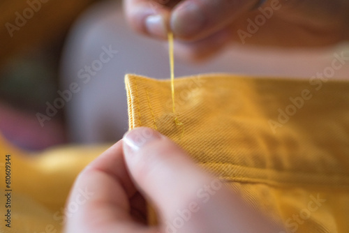 hands sewing on a button of a yellow jacket