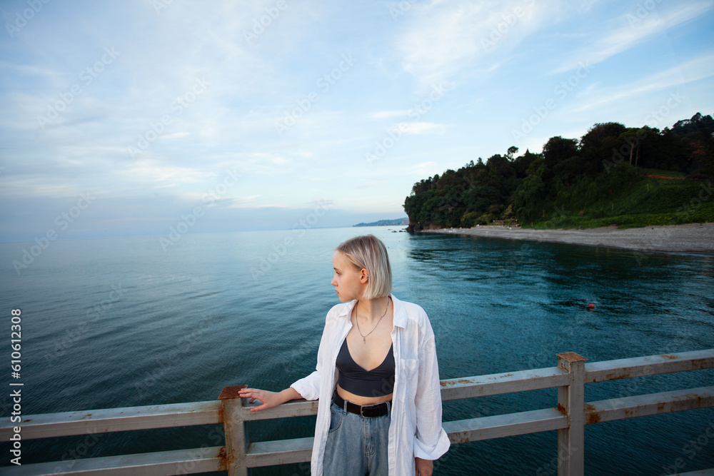 Young woman in white shirt standing on pier on the background of sea and sky