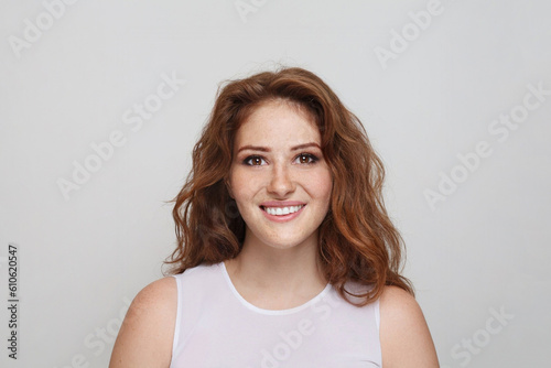 Portrait of cheerful redhead woman with healthy wavy ginger hair and fresh clear skin smiling on grey background