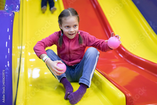Little smiling girl having fun on kids’ slide in amusement center for kids