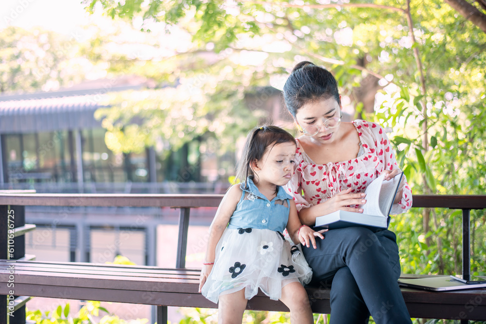Fototapeta premium Asian mom with laptop working on desk from home along with raising a small child.