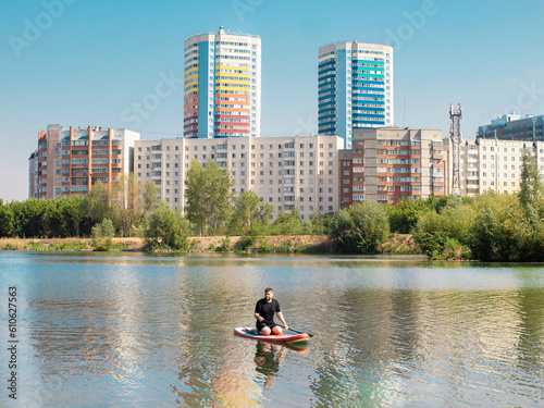 man rowing on paddle surf board SUP in the lake in the city among the houses