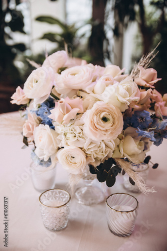 Wedding. Decor. Floristics. The festive table is decorated with a composition of pink and blue flowers with leaves of greenery. There are candles  glasses and plates on the table