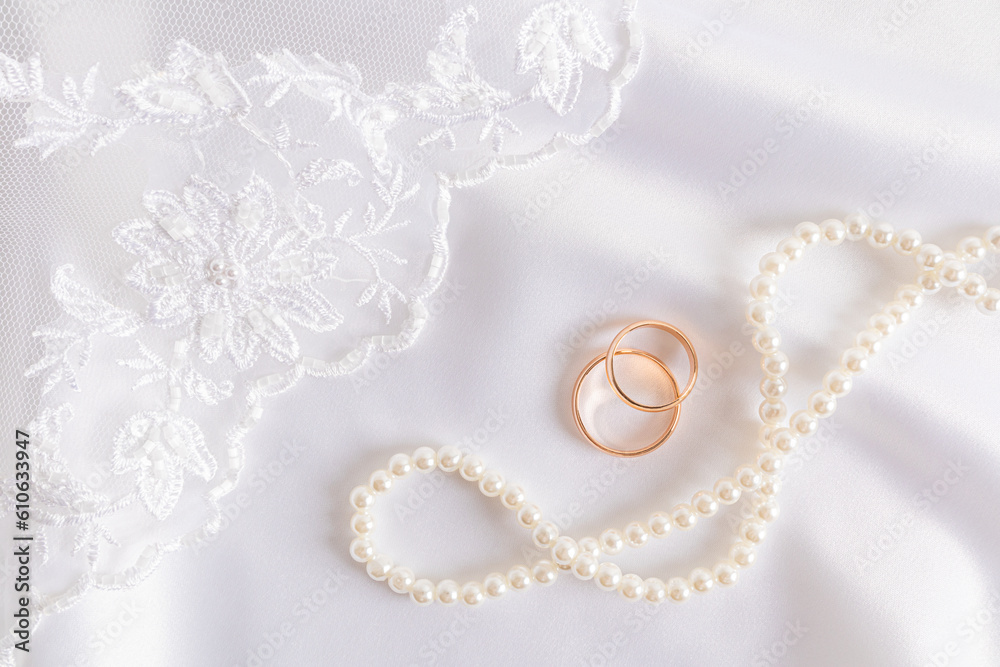 Beautiful wedding background. Two gold wedding rings on white satin with a richly embroidered bridal veil and pearl beads. postcard, cover.