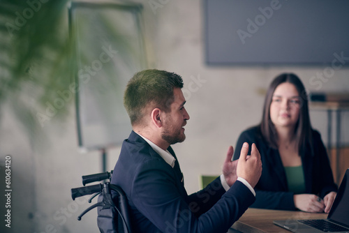 A wheelchair bound businessman confidently leads a business meeting in a large, modern office, exemplifying inclusive leadership, effective communication, and the power of diversity in driving success