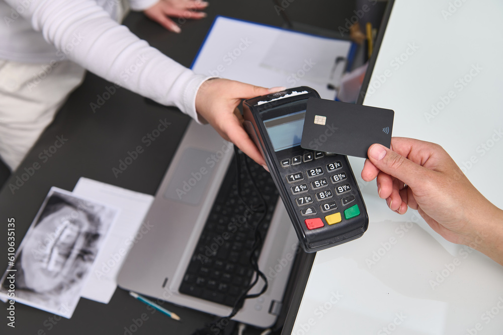 Top view customer hand holding a black mockup credit card above a POS terminal, making wireless or cashless payment using NFC technology. Close-up. Copy advertising space. People, business and finance Top view customer hand holding a black mockup credit card above a POS terminal, making wireless or cashless payment using NFC technology. Close-up. Copy advertising space. People, business and finance