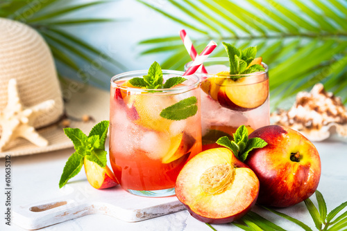 Peach cocktail, iced peach tea, fruit drink, summer beverage with fresh fruits and mint at tropical background..