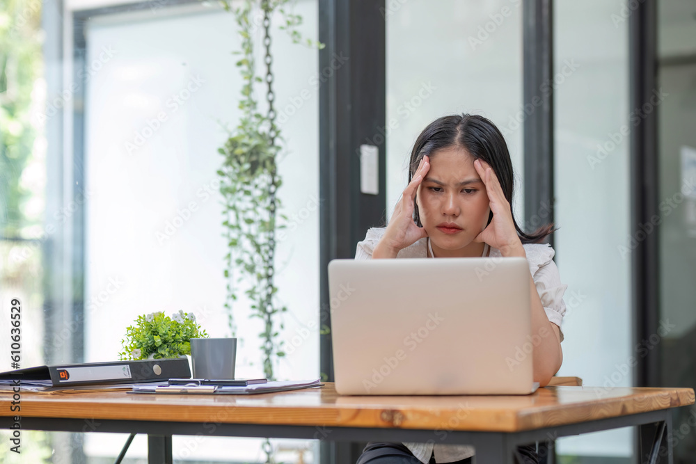 Young Asian businesswoman working on laptop computer, stressed has a headache and thinks hard from work at the office. Young Asian businesswoman working on laptop computer, stressed has a headache and thinks hard from work at the office.