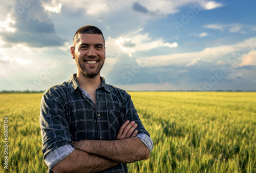 Portrait of young farmer standing in a green wheat field looking at camera.