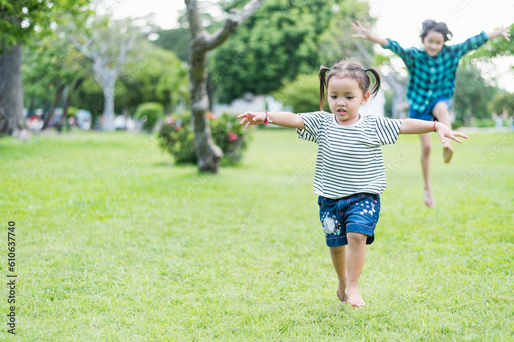 Happy girl running on green grass in the park Cheerful children in the meadow in the park under the sunlight. Child playing on spring grass, young woman's sprint at sunset in evening backyard.