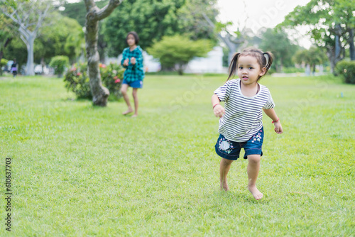 Happy girl running on green grass in the park Cheerful children in the meadow in the park under the sunlight. Child playing on spring grass, young woman's sprint at sunset in evening backyard. © Subhakitnibhat