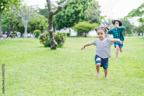 Happy girl running on green grass in the park Cheerful children in the meadow in the park under the sunlight. Child playing on spring grass, young woman's sprint at sunset in evening backyard.