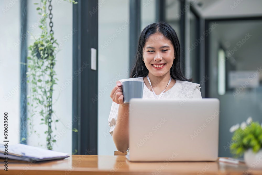 Beautiful young Asian businesswoman drinking a coffee working on laptop at office. Beautiful young Asian businesswoman drinking a coffee working on laptop at office.