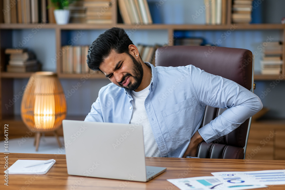Indian businessman working in office, having severe back pain, overtired worker working with laptop. Indian businessman working in office, having severe back pain, overtired worker working with laptop.