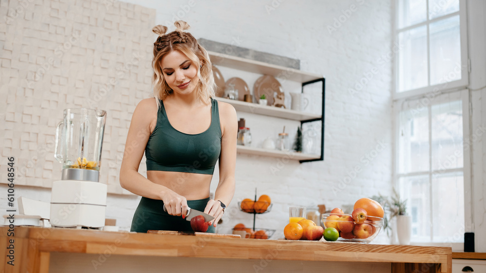Beautiful fitness woman in green sport clothing standing on kitchen and doing fresh orange juice