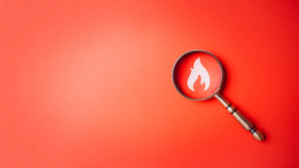 Fire surveillance inspection indicator and fire fighting with magnifying glass on red orange background. Fireman and conflagration concept. Wildfire and forest fire theme.