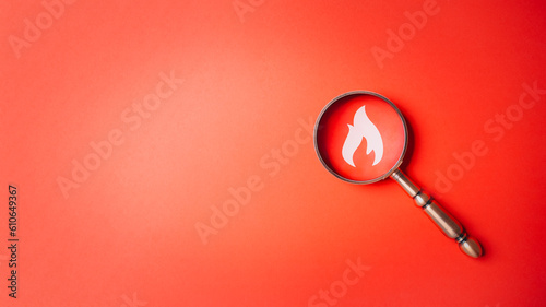 Fire surveillance inspection indicator and fire fighting with magnifying glass on red orange background. Fireman and conflagration concept. Wildfire and forest fire theme.