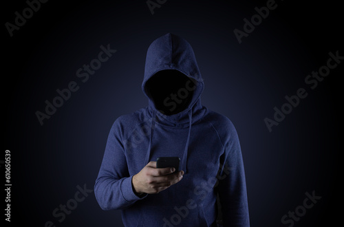 A hacker in a blue hood is holding a phone. Phone fraudster.