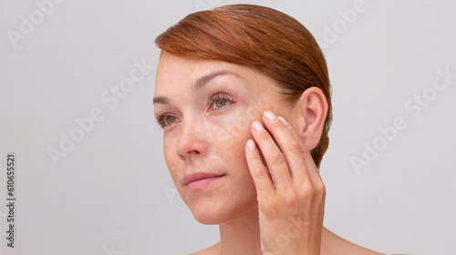 Portrait of cropped caucasian middle aged woman face with freckles touching skin by hand on white background looking aside photo