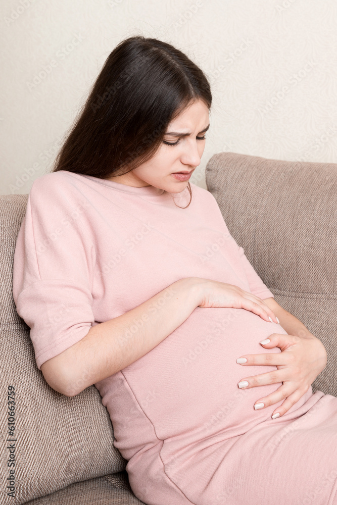 Pregnant Lady Having Massaging Lower belly Sitting On Sofa Indoor. Pregnancy Problems Concept. Maternity healthcare Pregnant Lady Having Massaging Lower belly Sitting On Sofa Indoor. Pregnancy Problems Concept. Maternity healthcare