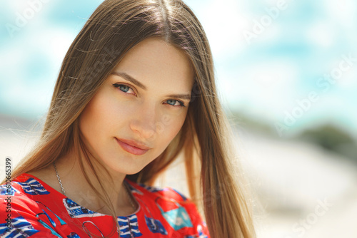 Portrait of a beautiful young girl in a red dress with blue eyes on a landscape background in a bokeh blur.