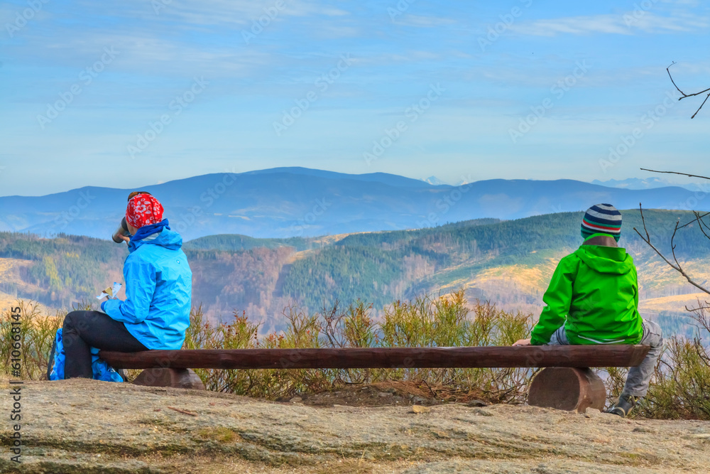 Two tourists (woman and child) admiring the mountain landscapes and resting on a wooden bench at Malinowska Skała on the hiking trail to Skrzyczne on an autumn sunny afternoon in Beskid Śląski, Poland