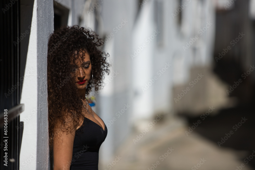 Obraz premium beautiful brunette woman with curly hair and elegant black dress is visiting a city of andalusia in the south of Spain. The city with white walls and typical mediterranean style.