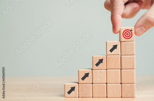Hand holding wooden block with target aiming dart board and arrow up on table background. Business achievement objective goal and project progress growth value processing marketing financial concept