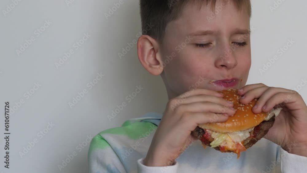 portrait of a handsome european boy eats a hamburger, white background, studio shot.a hungry schoolboy has breakfast with a burger. fast food, school meals