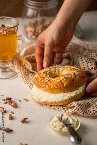 mano de mujer sosteniendo un pan partido por la mitad con queso crema y una bebida caliente photo
