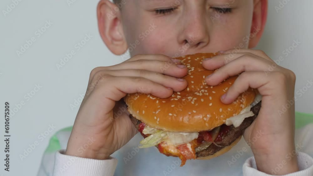 portrait of a handsome european boy eating a big appetizing hamburger and closing his eyes in pleasure. fast food concept, boy eating burger portrait of a handsome european boy eating a big appetizing hamburger and closing his eyes in pleasure. fast food concept, boy eating burger