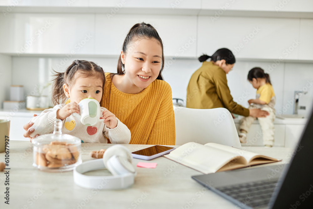 Happy Asian mom watching cartoon with her kid on laptop while they sitting at table in the kitchen Happy Asian mom watching cartoon with her kid on laptop while they sitting at table in the kitchen