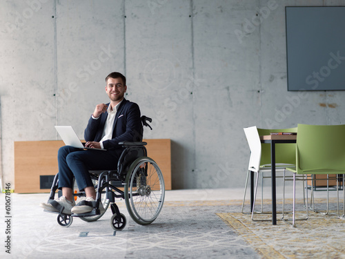 A businessman with disability in a wheelchair using laptop in a modern office