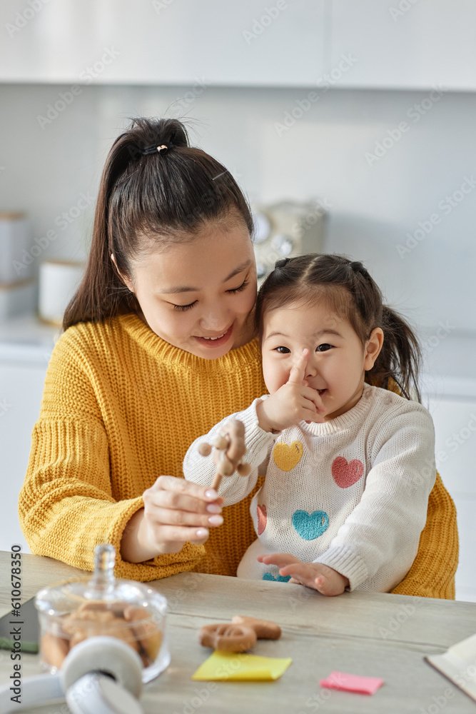 Vertical image of Asian happy mom playing with her little daughter in the kitchen Vertical image of Asian happy mom playing with her little daughter in the kitchen