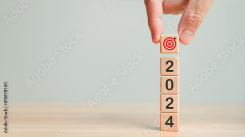 Hand stacking 2024 goal target with dartboard icon in New Year 2024 celebration. Wooden cubes target icon symbol table background. Business planning development strategy. Future achievement concept.
