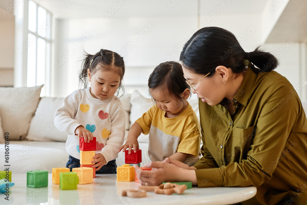 Asian young mom sitting with her children in the room while they playing toys Asian young mom sitting with her children in the room while they playing toys
