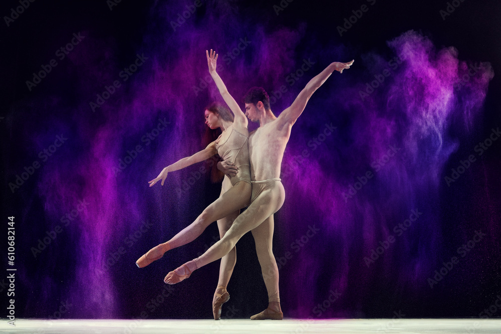 Obraz premium Beautiful, artistic young man and woman, professional ballet dancers performing with colorful powder splashes over black studio background. Art, festival, beauty of dance, inspiration, youth concept